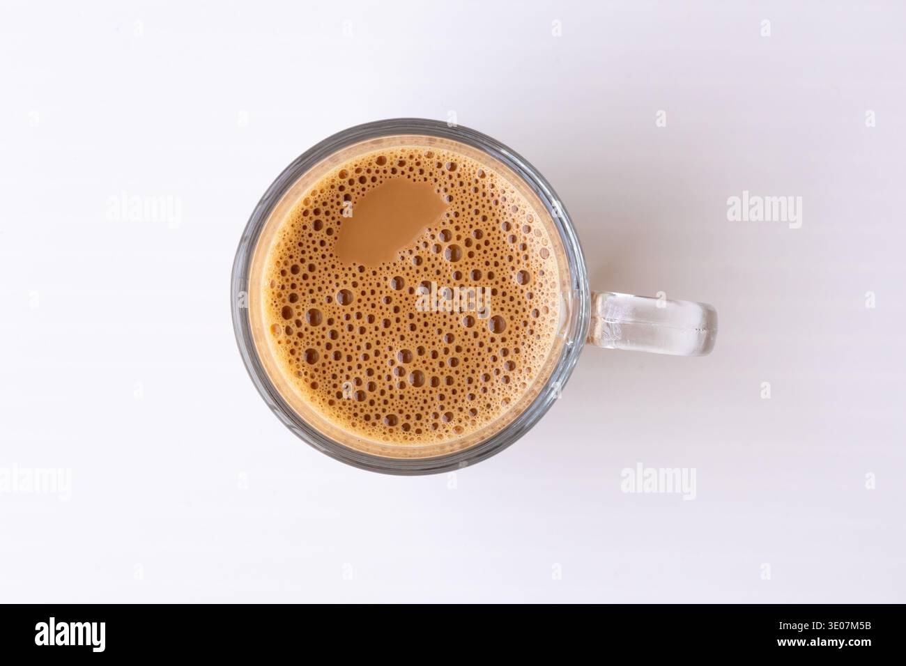 Scatto ad angolo alto di una tazza di vetro trasparente riempita con tè caldo al latte con consistenza schiumosa isolata su sfondo bianco. Perfetto per i menu delle bevande, CA Foto Stock