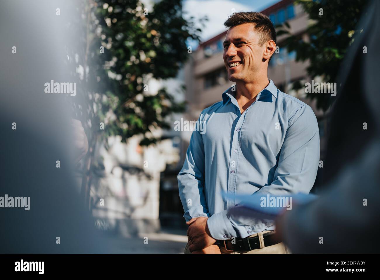 L'uomo d'affari sorride mentre si trova all'aperto con una camicia azzurra Foto Stock
