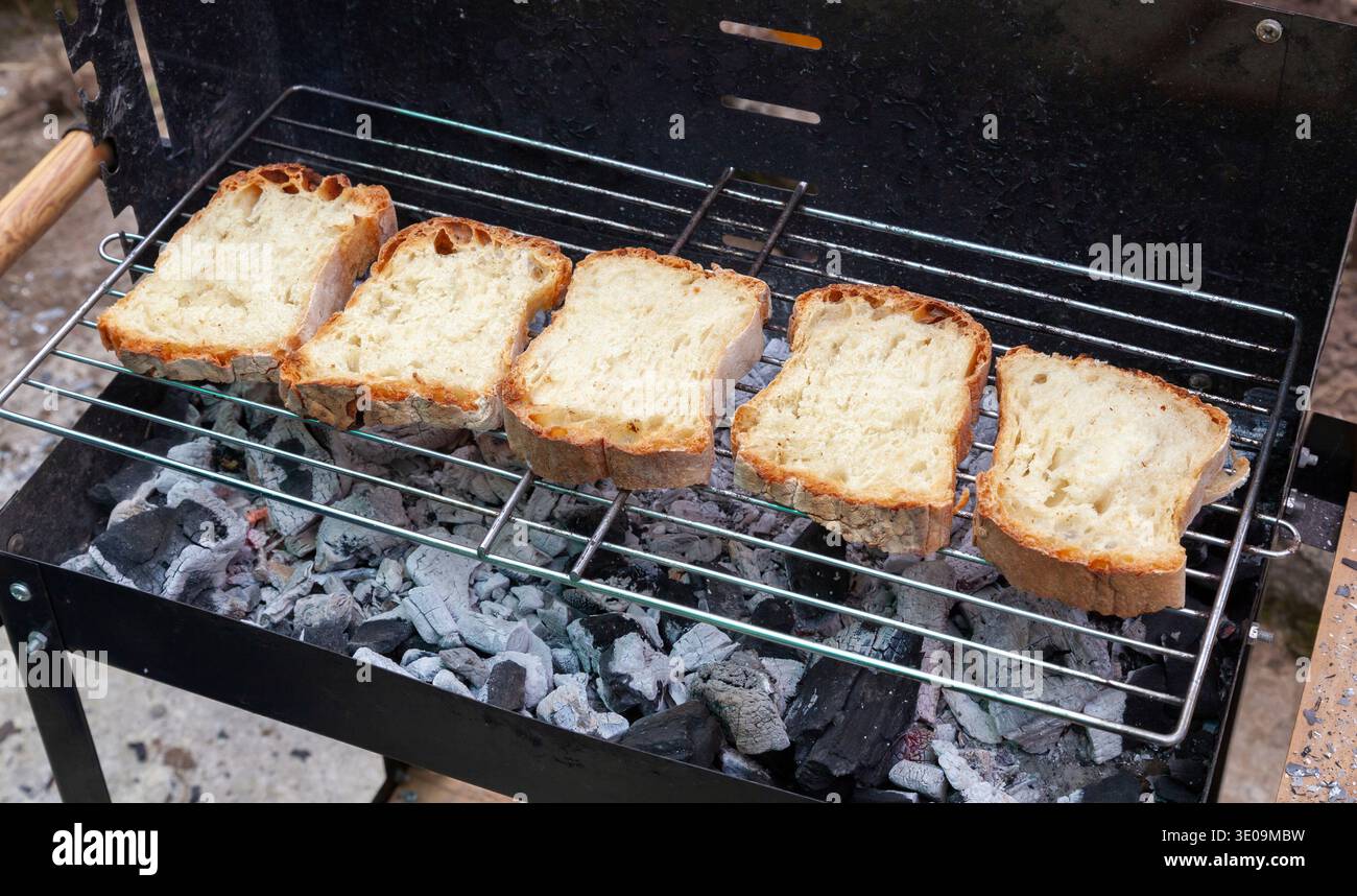 Cinque fette di pane stanno tostando su un barbecue con sotto i carboni caldi Foto Stock