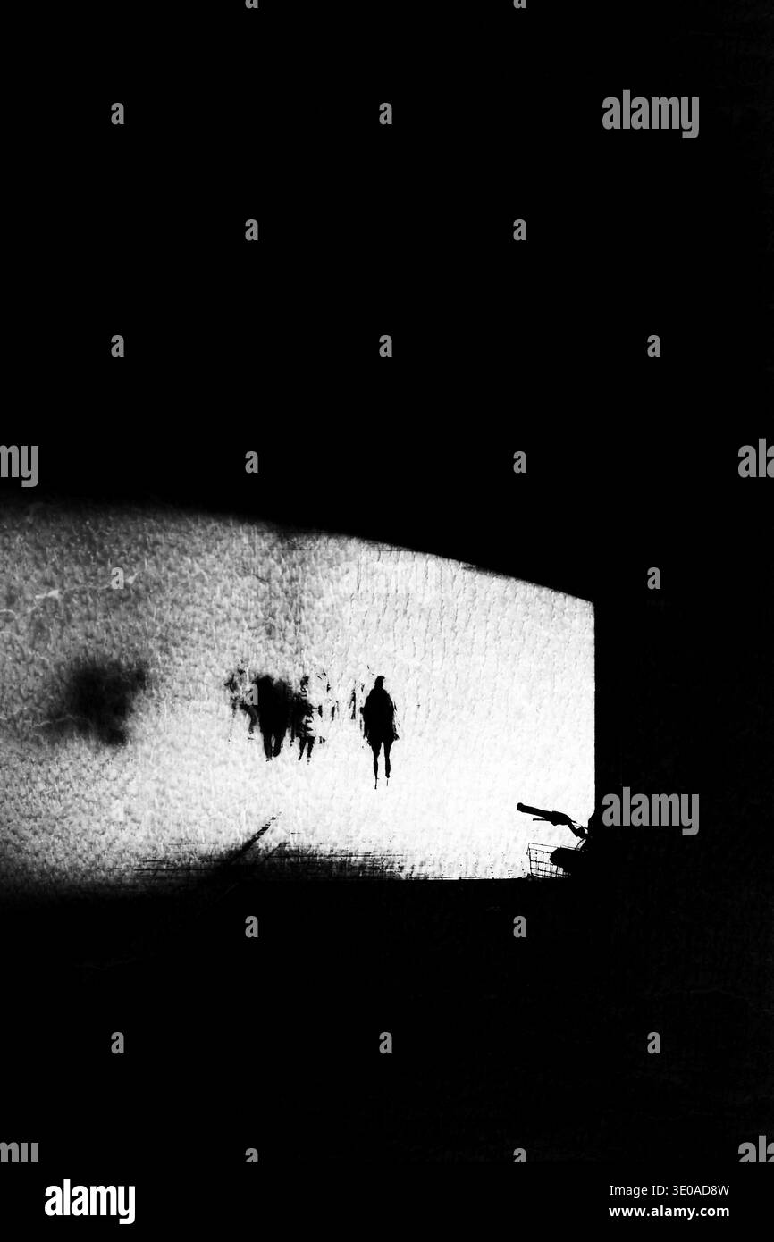 Foto sperimentale in bianco e nero, sagome scure distorte di figure che si muovono attraverso un vuoto rettangolare chiaro e netto circondato da ombre profonde. Foto Stock