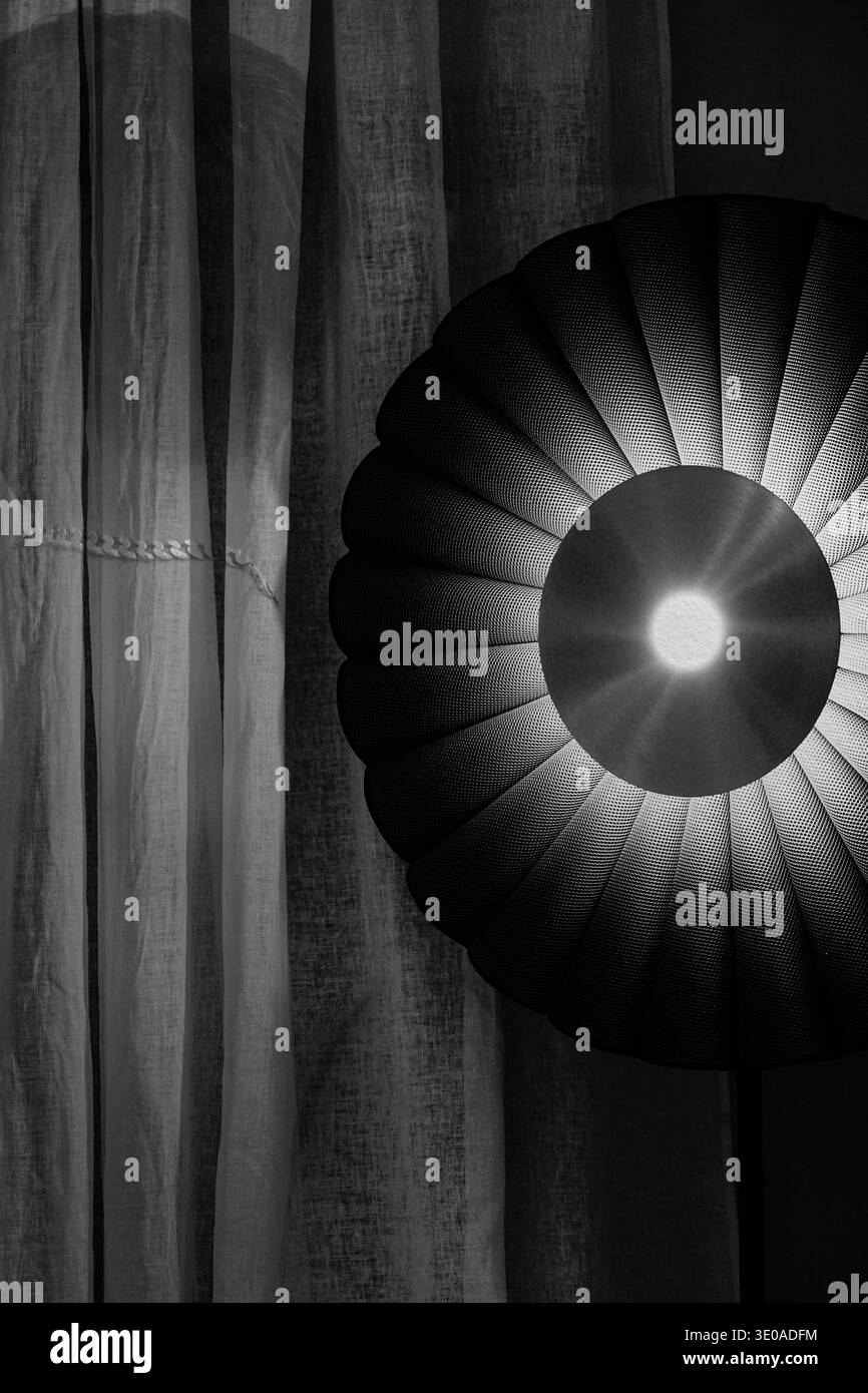 Studio ravvicinato monocromatico di un paralume a pieghe radiali con illuminazione centrale luminosa e tende di lino. Foto Stock