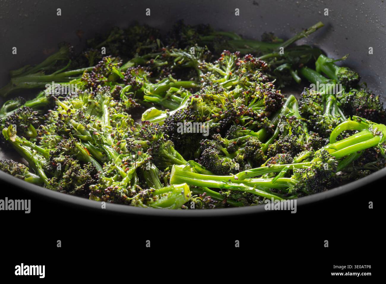 Broccoli germogliati di viola friggono in uno sfondo di una padella ceramica profonda. Foto Stock