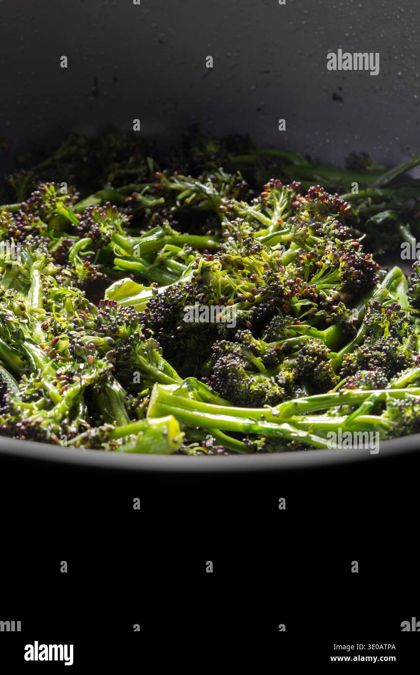Broccoli germogliati di viola friggono in uno sfondo di una padella ceramica profonda. Foto Stock