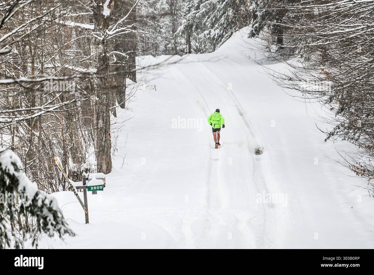 Catturato tra due stagioni, il corridore sale su una collina in North Street a East Montpelier, Vermont, USA, dopo una tempesta di neve di fine stagione. Foto Stock