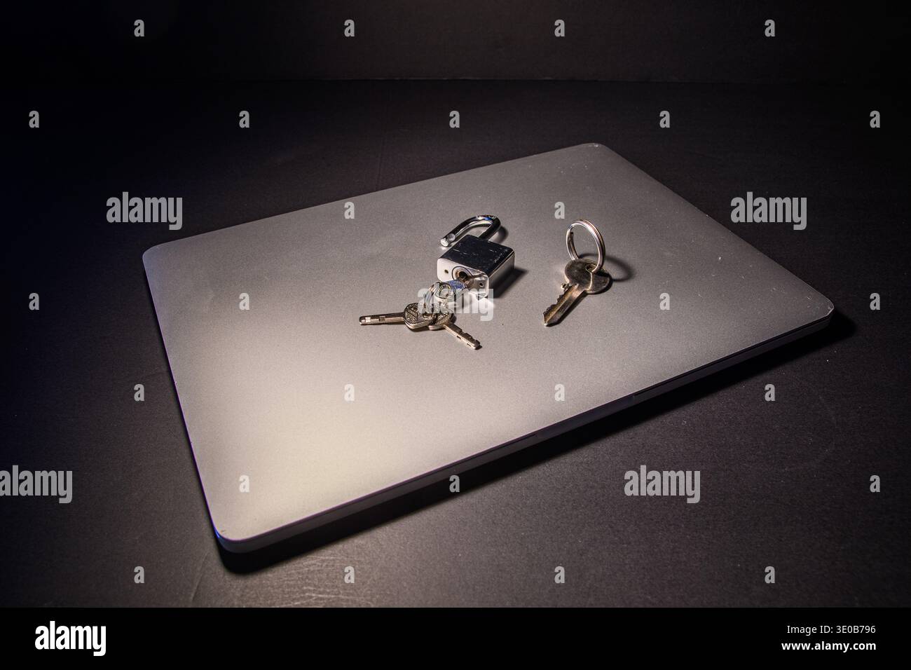 Lucchetto e chiavi aperti su un notebook chiuso, immagine concettuale della sicurezza informatica, gestione degli accessi, sicurezza dei dispositivi e potenziale vulnerabilità nel digitale Foto Stock