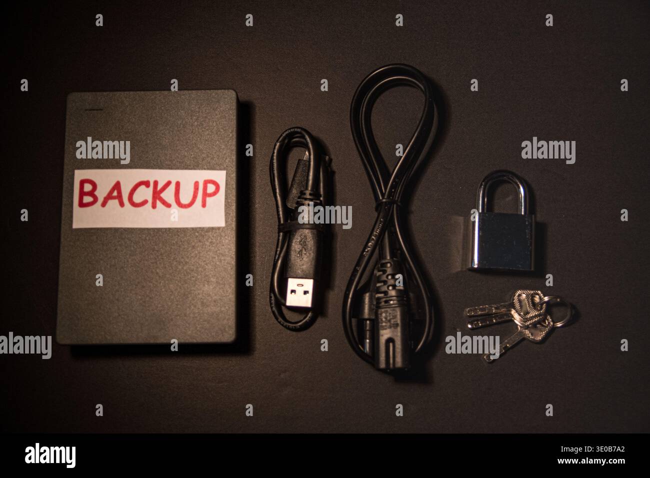 Unità di backup esterna con cavi, lucchetto e chiavi su una scrivania scura, immagine concettuale di backup sicuro, archiviazione protetta, crittografia e sicurezza dei dati Foto Stock