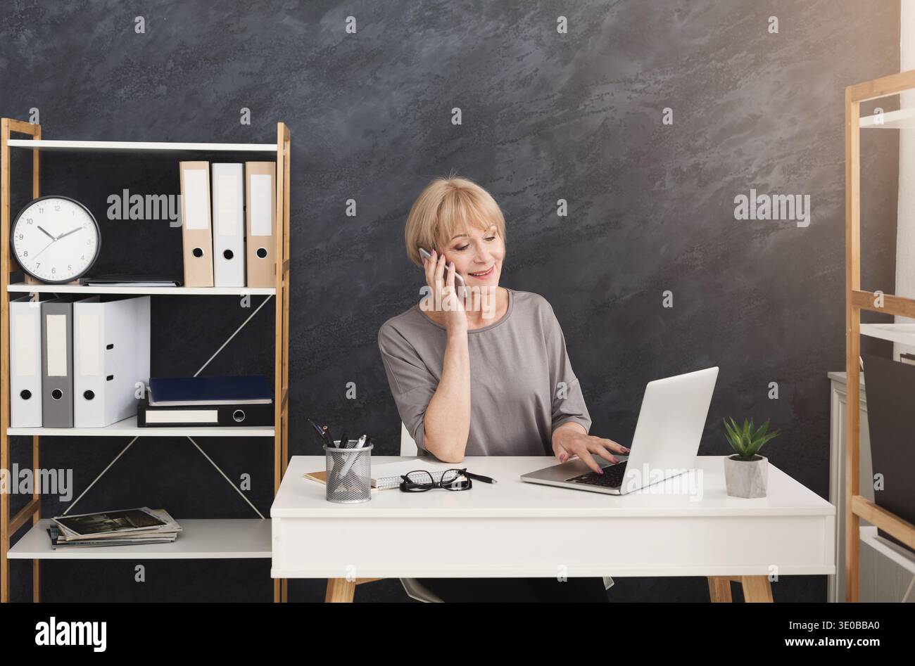 Felice donna d'affari di mezza età al lavoro che parla al telefono Foto Stock