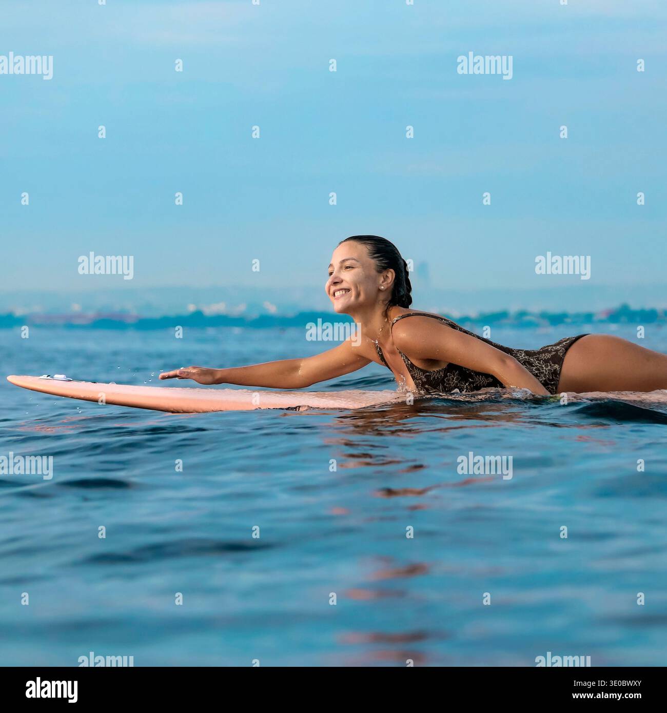 Giovane donna che trasmette in tavola da surf Near Shore, Lifestyle Capture con Bright Mood, Coastal Sky e coinvolgente Foto Stock