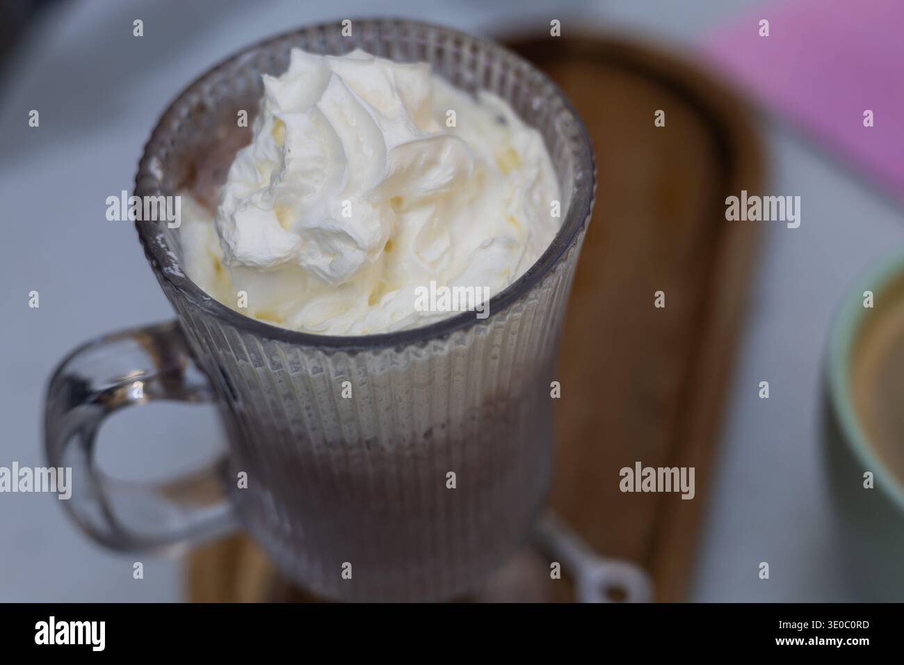 un alto bicchiere di ricca cioccolata calda condita da un generoso vortice di panna montata. servito su un vassoio di legno per un'atmosfera intima e appagante da caffe' Foto Stock