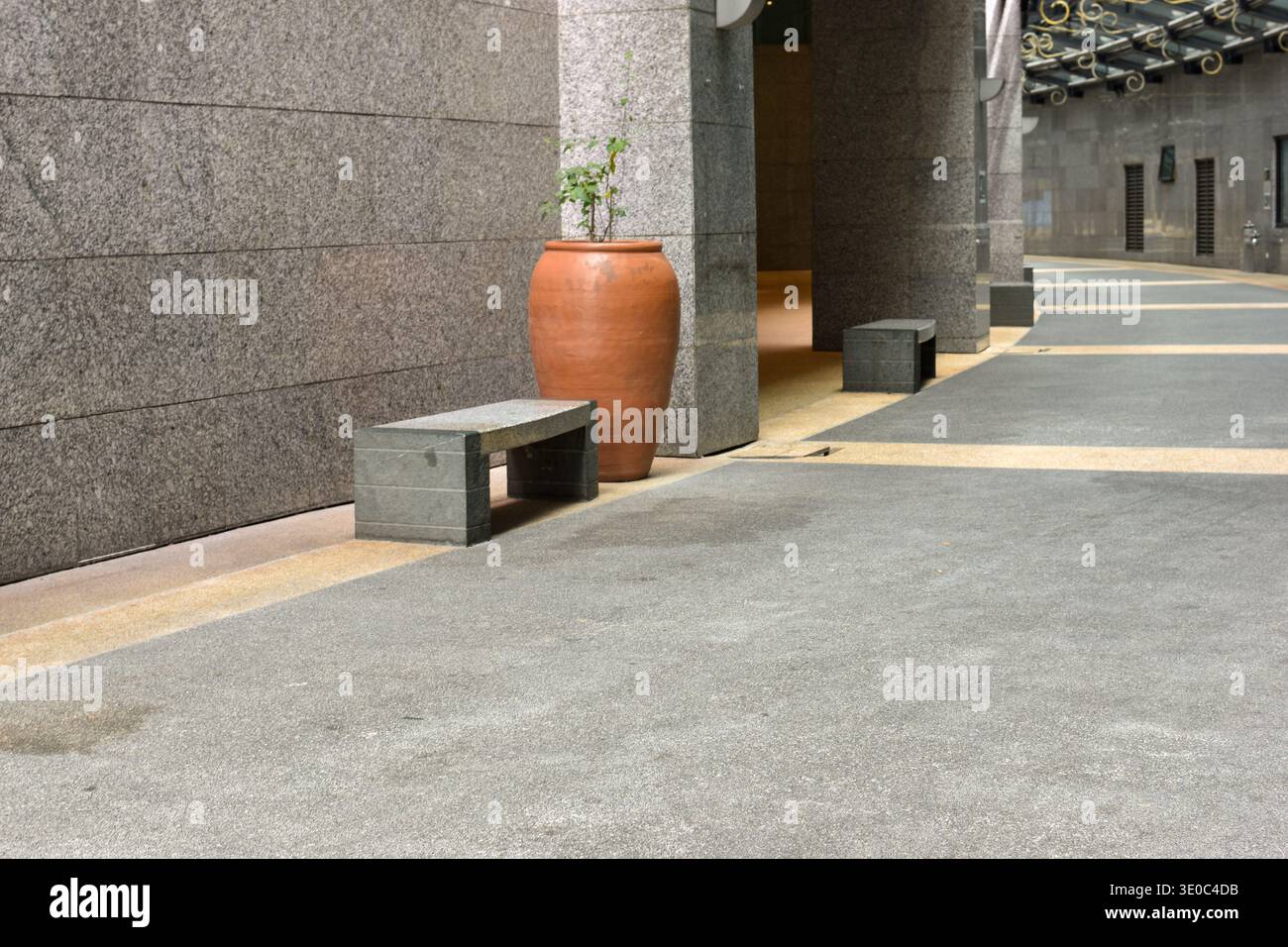 Putrajaya, Malesia - 15 novembre 2025: Corridoio di granito con pavimento in pietra lucida, panchine allineate, vaso di piante di terracotta Foto Stock