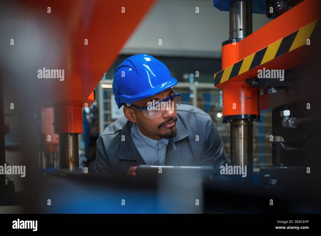 L'ingegnere industriale afroamericano controlla le apparecchiature delle macchine per il controllo di qualità e la manutenzione in un ambiente di produzione molto trafficato. Foto Stock