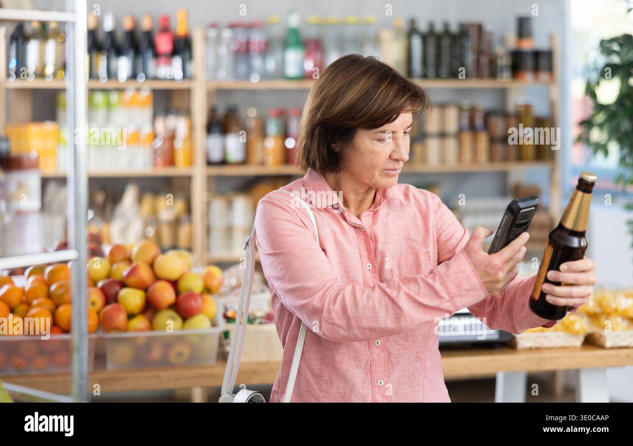 L'acquirente donna esegue la scansione del codice QR sull'etichetta della birra nel negozio di alimentari Foto Stock