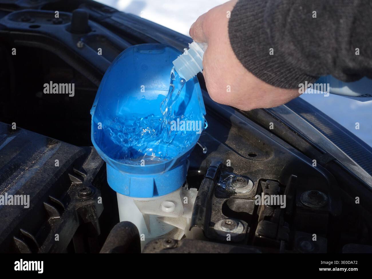 15.02.2025, Germania, Berlino, Berlino - foto simbolica: Il liquido lavaparabrezza viene versato nel serbatoio di un lavaparabrezza nel gruppo motore Foto Stock