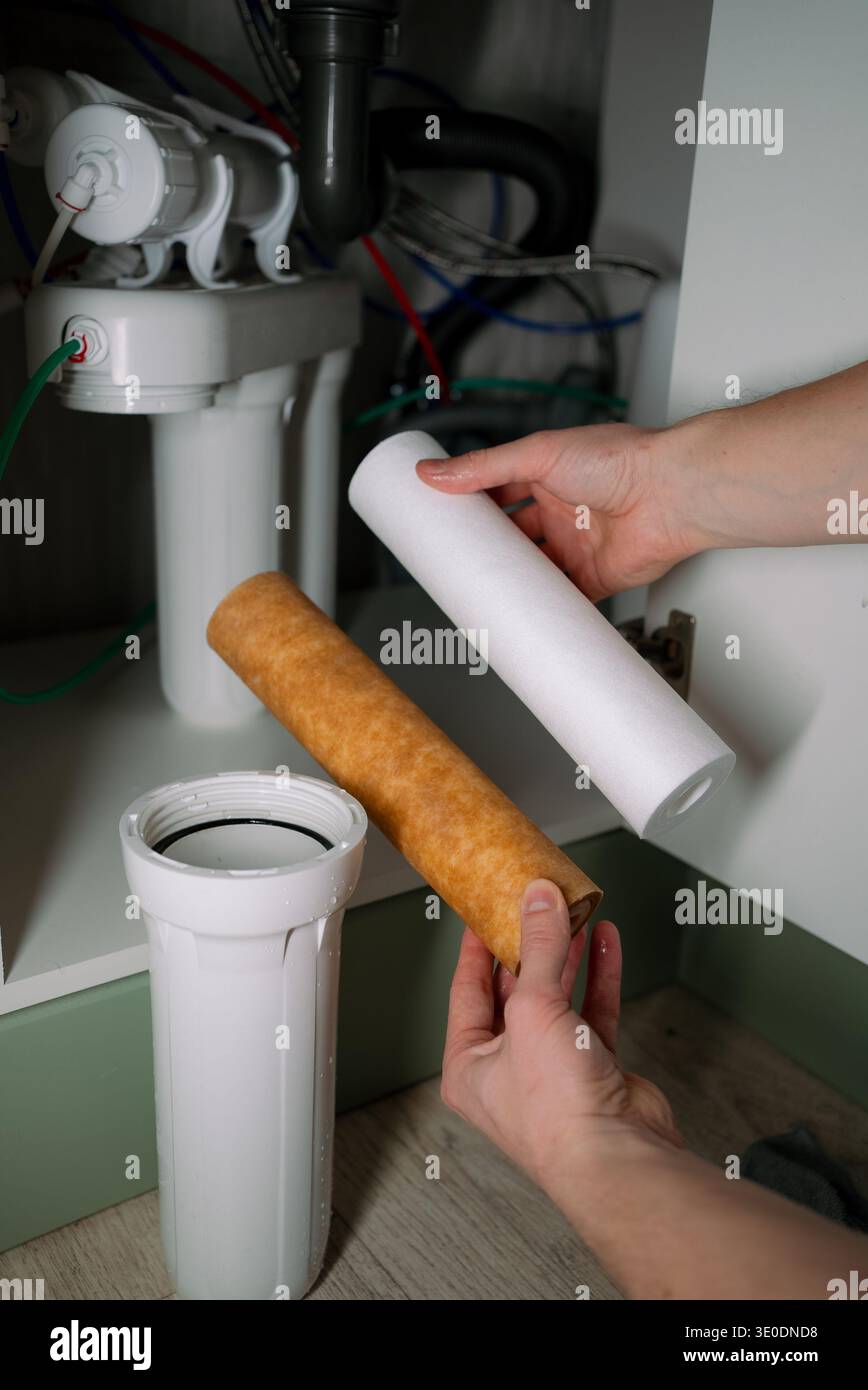 Sostituzione delle mani di un filtro dell'acqua di sedimenti sporco per una sostituzione pulita in un sistema di osmosi inversa sotto il lavandino, che mostra la manutenzione per migliorare la qualità e l'igiene dell'acqua potabile domestica Foto Stock
