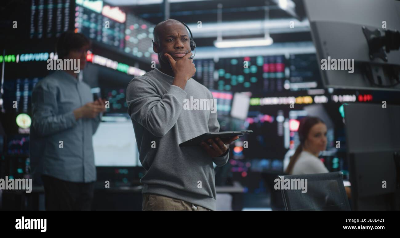 Diversi broker azionari che utilizzano i segnali manuali e i gesti nel pozzo di trading eseguono ordini di acquisto e vendita istantanei. Commerciante afro-americano in supporti per cuffie, aumento del segnale della mano, possesso di un tablet digitale. Foto Stock