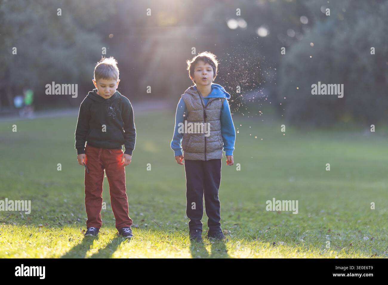 Ragazzi che giocano all'aperto, una che soffia particelle d'acqua alla luce del sole in un parco naturale Foto Stock