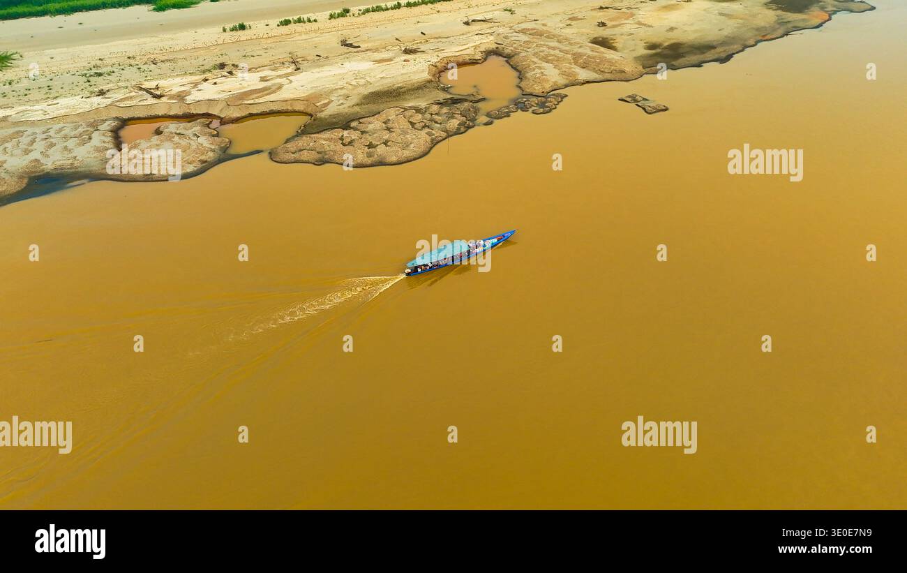 Vista aerea di una barca che naviga sul torbido fiume in contrasto con le consistenze della sponda erosa del fiume, Puerto Maldonado, madre de Dios, Perù. Foto Stock