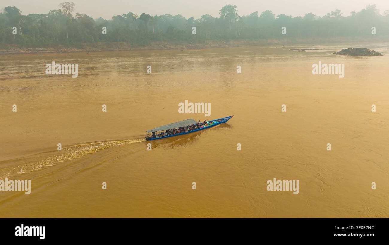 Vista aerea di una piccola barca che attraversa le torbide acque del fiume, incorniciata dal lontano verde della foresta pluviale amazzonica, Puerto Maldonado, madre de D. Foto Stock