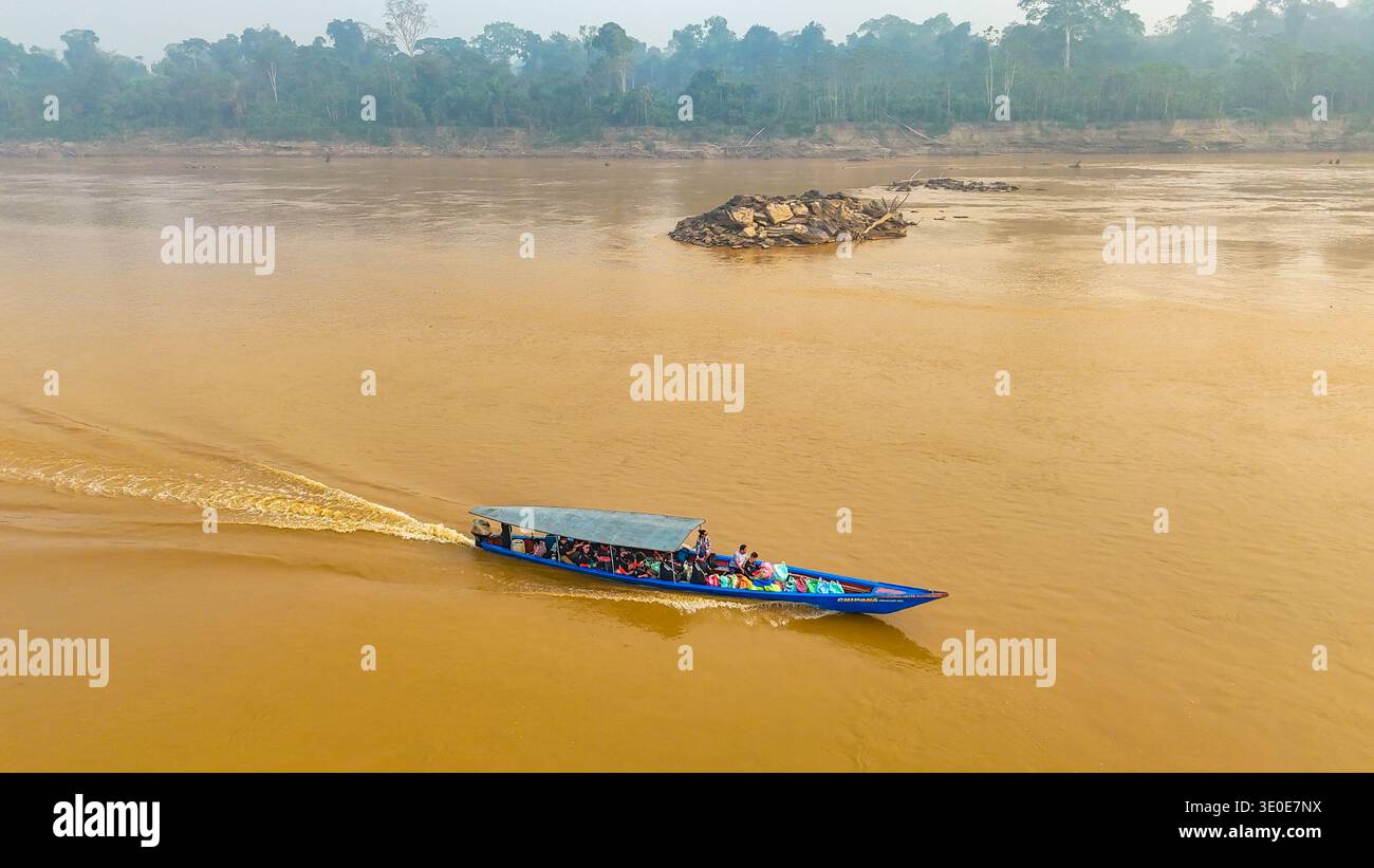 Vista aerea di una lunga barca blu attraversa il fiume fangoso, trasportando persone vicino a un affioramento roccioso, Puerto Maldonado, madre de Dios, Perù. Foto Stock