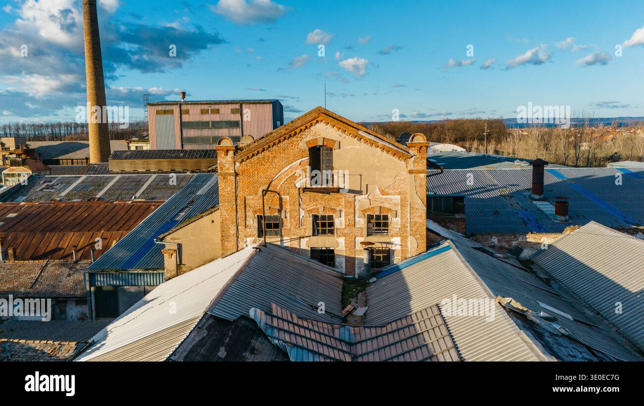 Vista aerea degli edifici industriali con pareti in mattoni rossi, tetti in metallo ondulato e un alto camino che perfora lo skyline, Sremska Mitrovica, Vojvodin Foto Stock