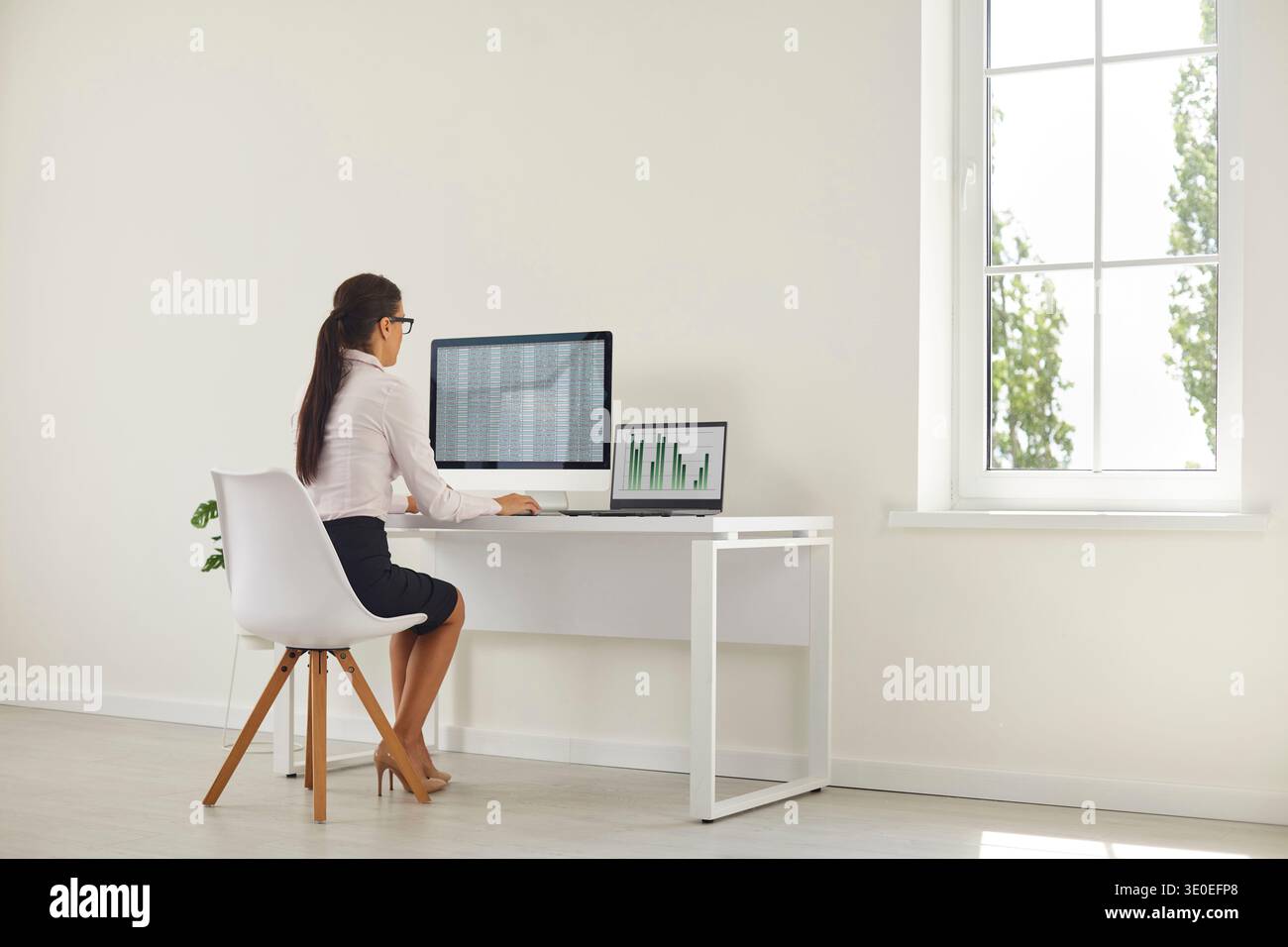 Analista donna che lavora al budget in ufficio domestico con monitor desktop e laptop Foto Stock