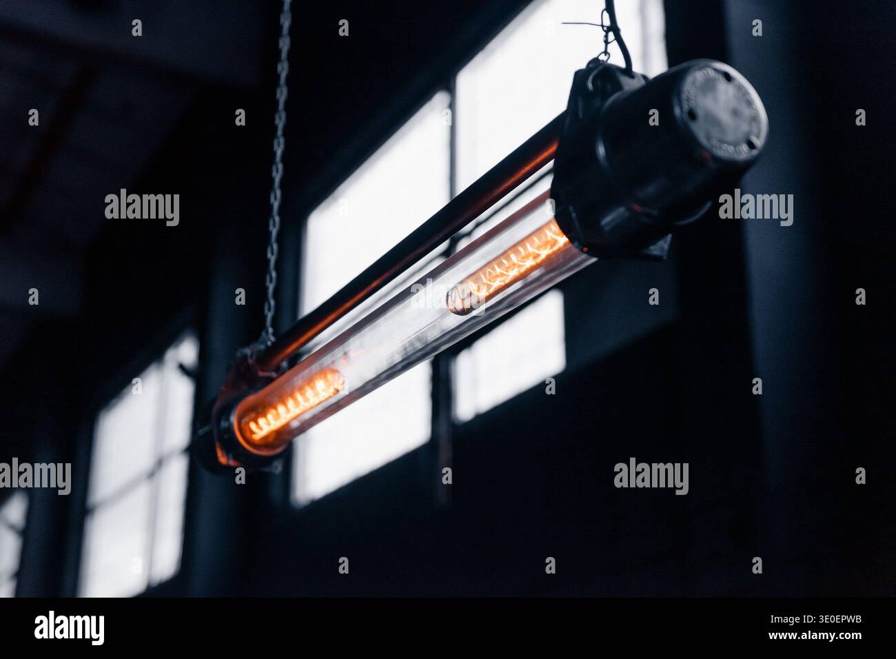 Lampada a sospensione a tubo vintage industriale. Uno scatto ravvicinato e poco luminoso di una lampada a sospensione a filamento tubolare in stile industriale appesa a catene in officina. Foto Stock