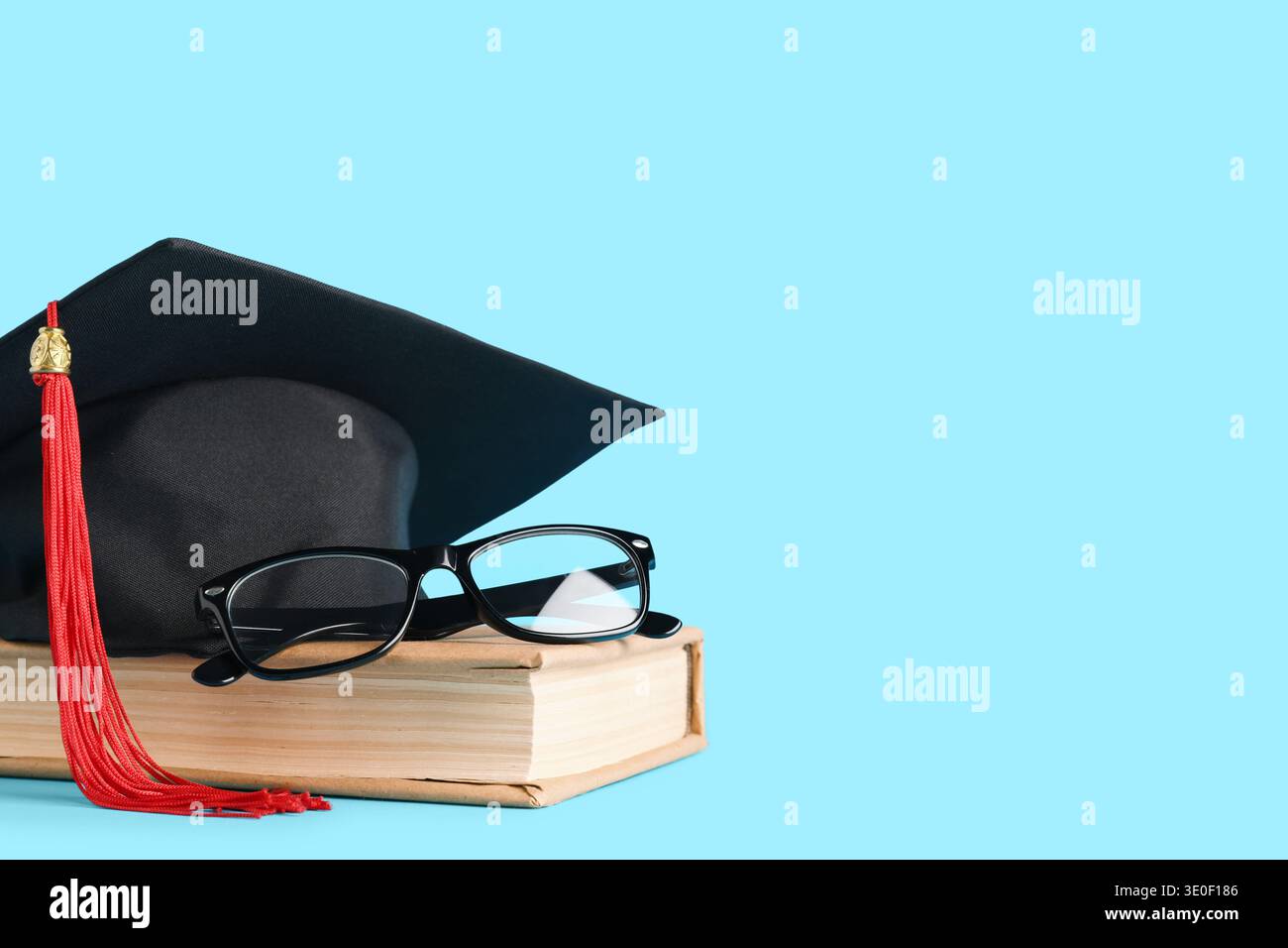 Cappello di graduazione, libro e occhiali su sfondo blu Foto Stock