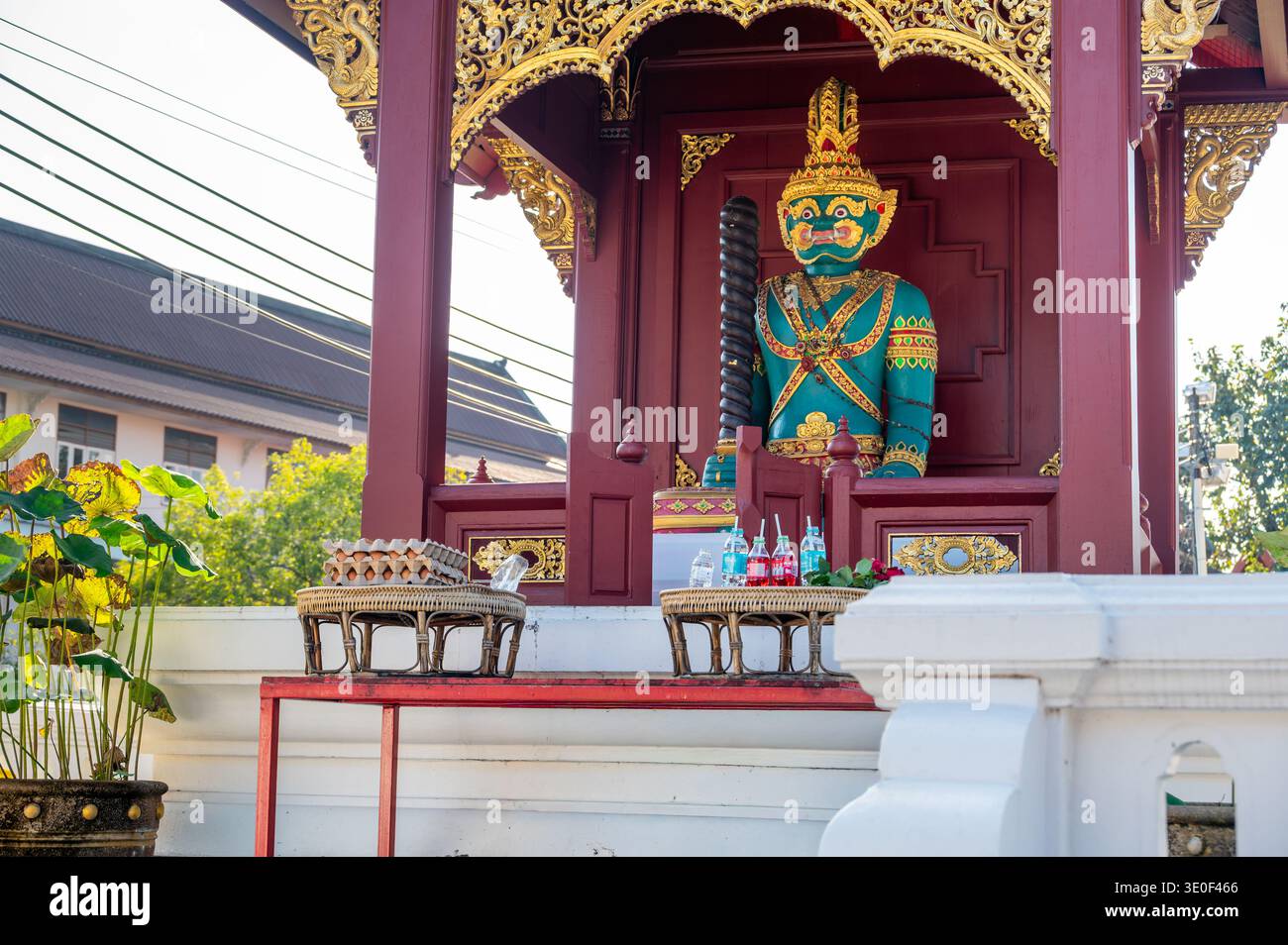 Statua del guardiano del tempio verde con offerte di soda e uova sul tavolo di fronte. Tradizionale rituale thailandese che simboleggia rispetto, fede e benedizioni in s Foto Stock