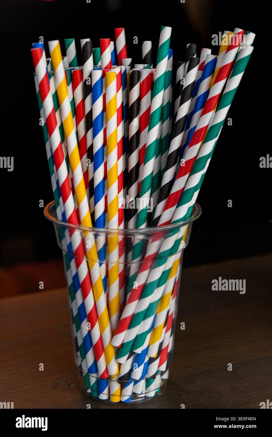 Una tazza di vetro trasparente che contiene cannucce colorate per bere carta con un design colorato a spirale. Foto Stock