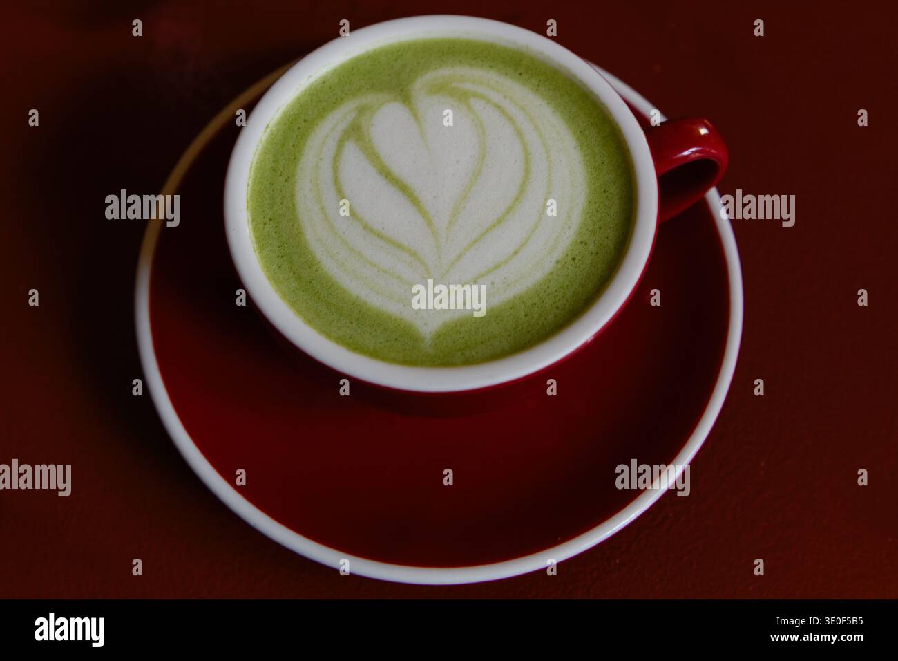 Tazza di tè matcha rosso e ceramica e piattino con cuore di latte in schiuma sulla superficie del tè. Il Matcha è una polvere finemente macinata di tè verde, specialmente proc Foto Stock