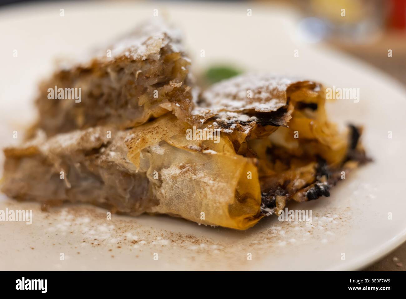 deliziose fette di strudel di mele dorate spolverate con zucchero a velo su un piatto bianco, con strati croccanti di fillo e un caldo ripieno di frutta dolce Foto Stock