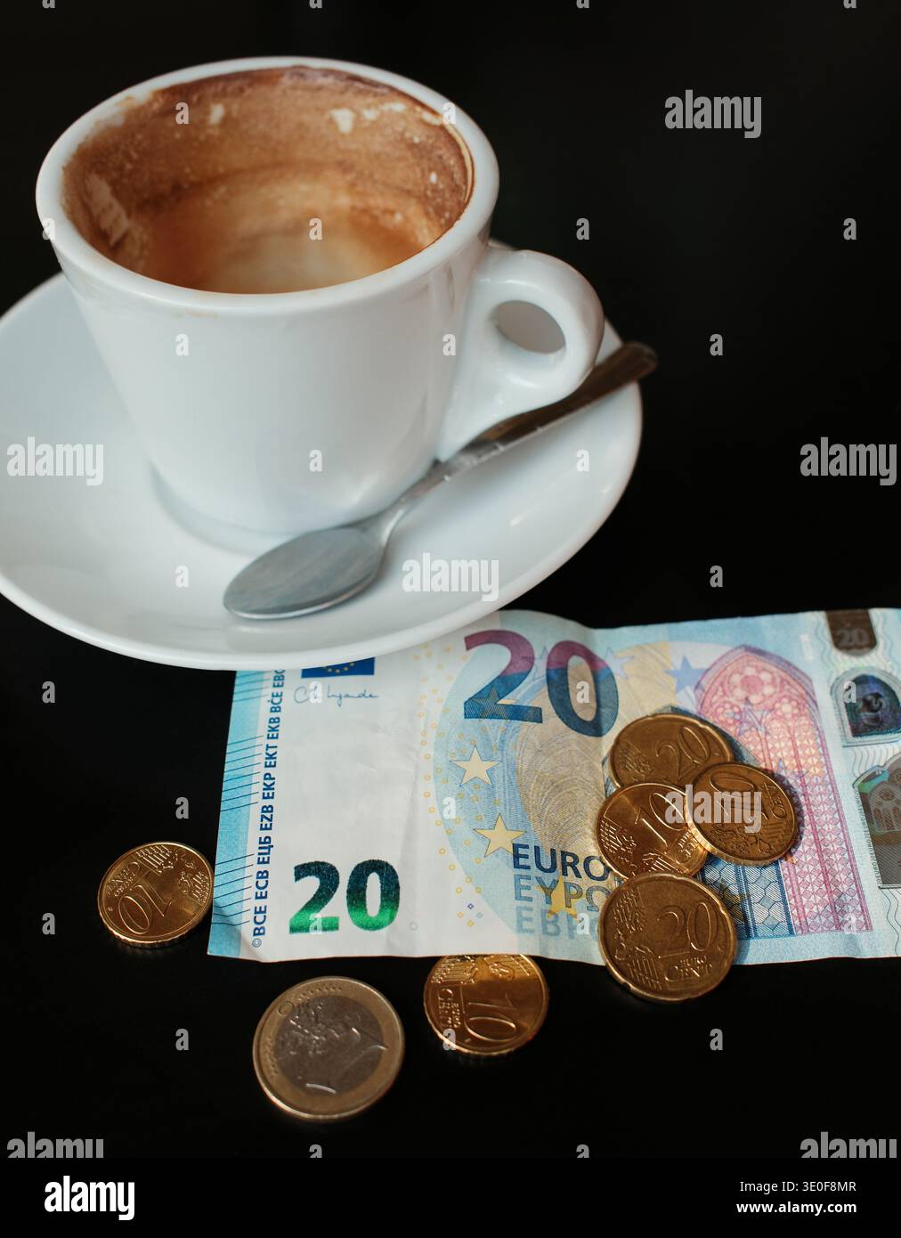 Cappuccino parzialmente bevuto in tazza bianca con banconota e monete in euro su tavolo scuro. Concetto di pagamento al bar, prezzo del caffè e spese quotidiane in Foto Stock