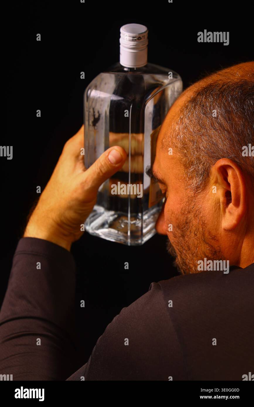 Uomo anziano che tiene una bottiglia in un momento di disperazione silenziosa, che riflette il peso emotivo della dipendenza, della solitudine e della tranquilla lotta dell'invecchiamento Foto Stock