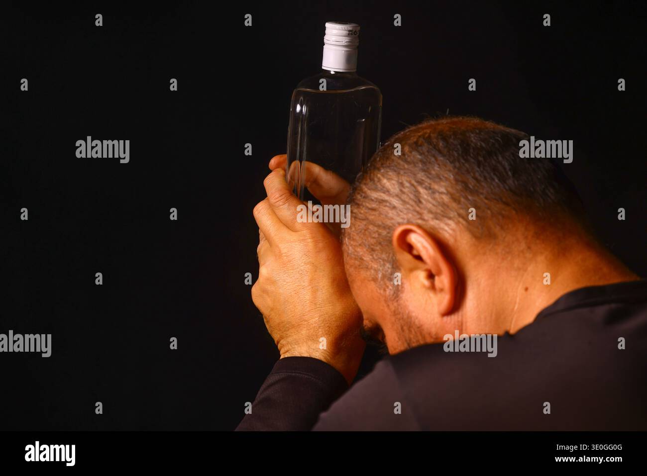 Uomo anziano che tiene una bottiglia in un momento di stanchezza emotiva, che riflette il peso della solitudine, della dipendenza e della tranquilla lotta dell'invecchiamento in è Foto Stock