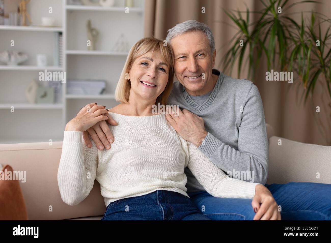 Una coppia matura che posa insieme sul divano di casa, sorridendo alla telecamera Foto Stock