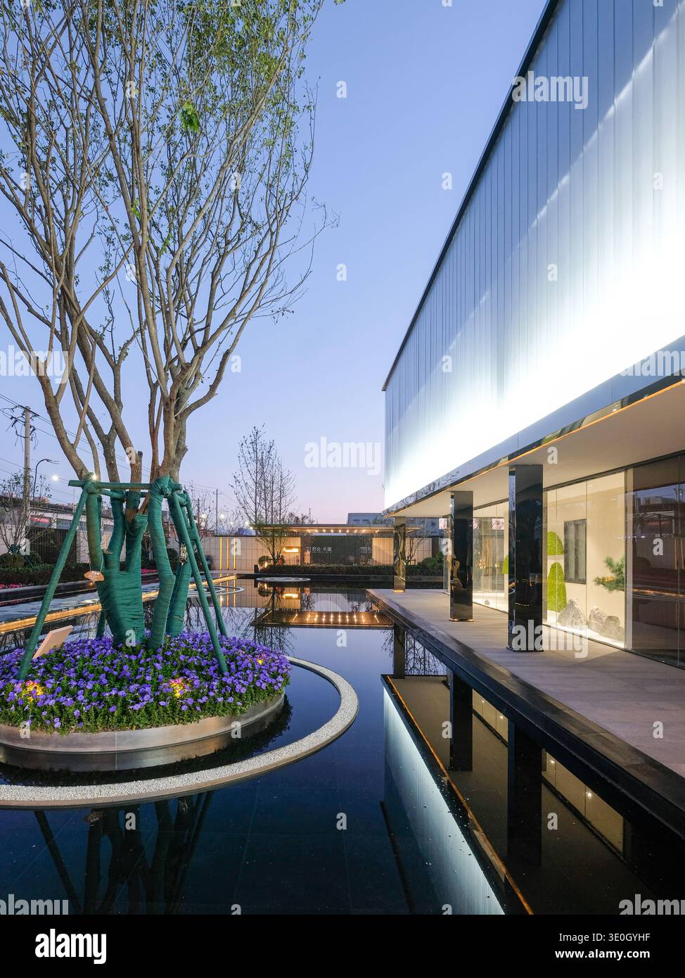 Descrizione: Una prospettiva verticale che mostra una moderna disposizione del giardino con giochi d'acqua e passaggi illuminati che conducono a un elegante edificio. L'i Foto Stock