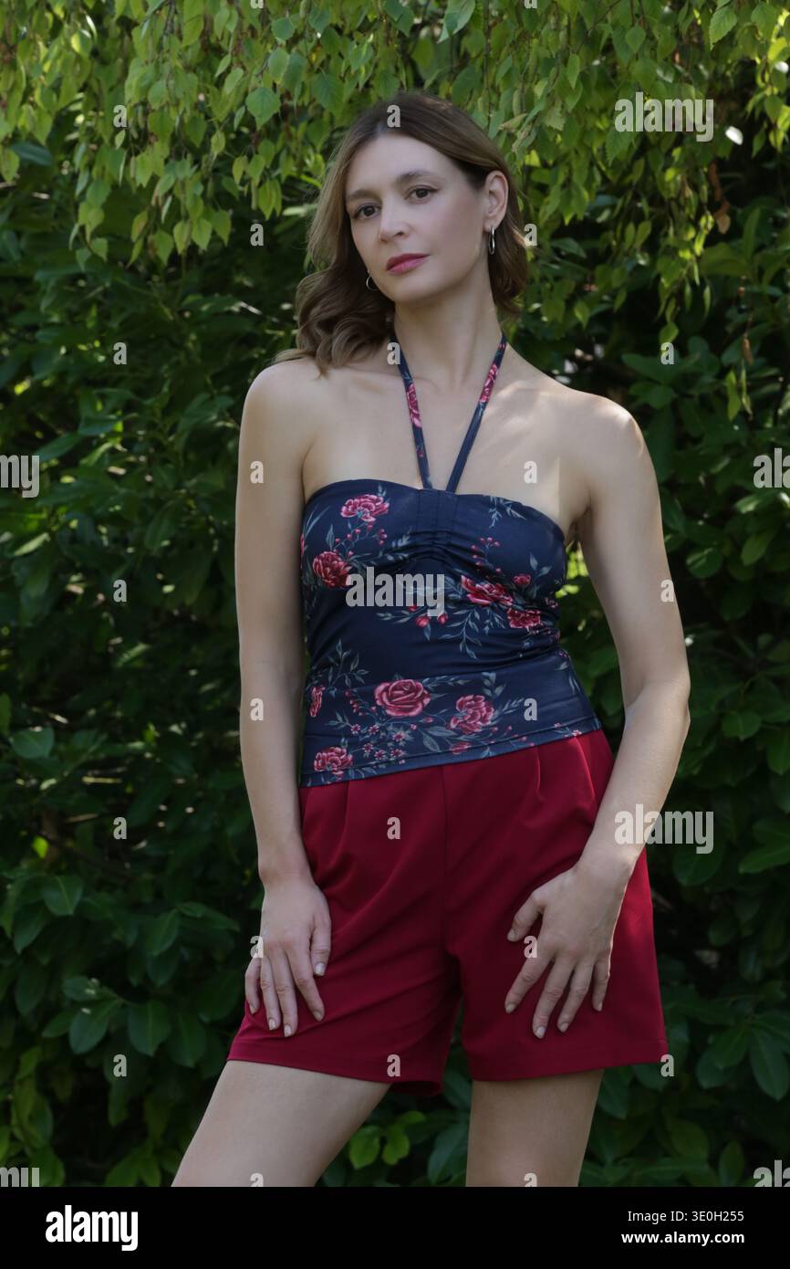 Modello di moda in tubolare scuro con collo a mandrino floreale e pantaloncini sartoriali rossi: Elegante concetto di Ritratto estivo e casual Fashion Foto Stock