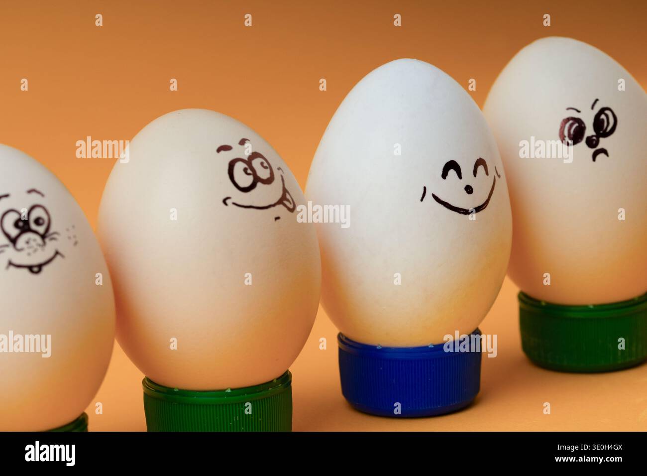 Simpatici personaggi dell'uovo di Pasqua con diverse espressioni facciali su sfondo arancione. Concetto di lavoro di squadra, diversità sociale o un gruppo di amici. Foto Stock