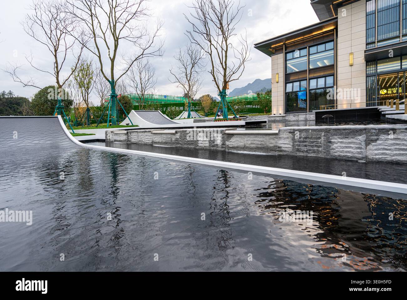 Una serena fontana con gradini in pietra che conducono ad un edificio moderno. L'immagine trasmette l'architettura del giardino, la tranquillità e il design strutturato. Foto Stock