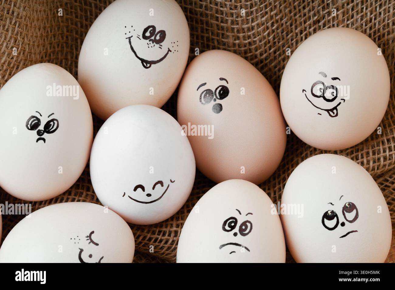 Gruppo di uova bianche con diverse espressioni facciali su sfondo burlap. Un'immagine concettuale che rappresenta gruppi sociali, diversità, salute mentale, a. Foto Stock