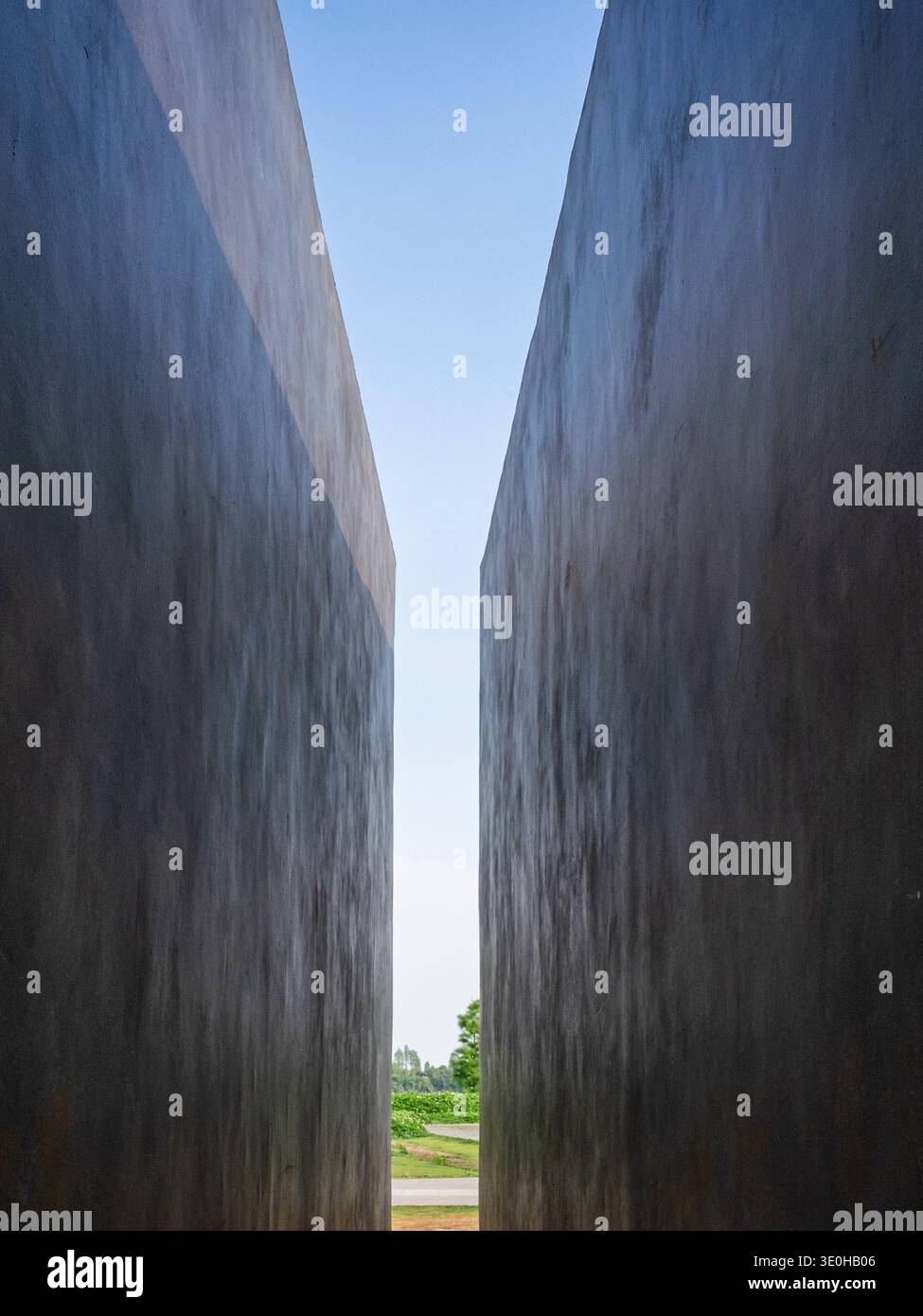 Una vista prospettica tra due massicce pareti minimaliste che guardano verso un frammento di cielo blu. L'immagine trasmette la prospettiva spaziale, l'architettura e la m Foto Stock