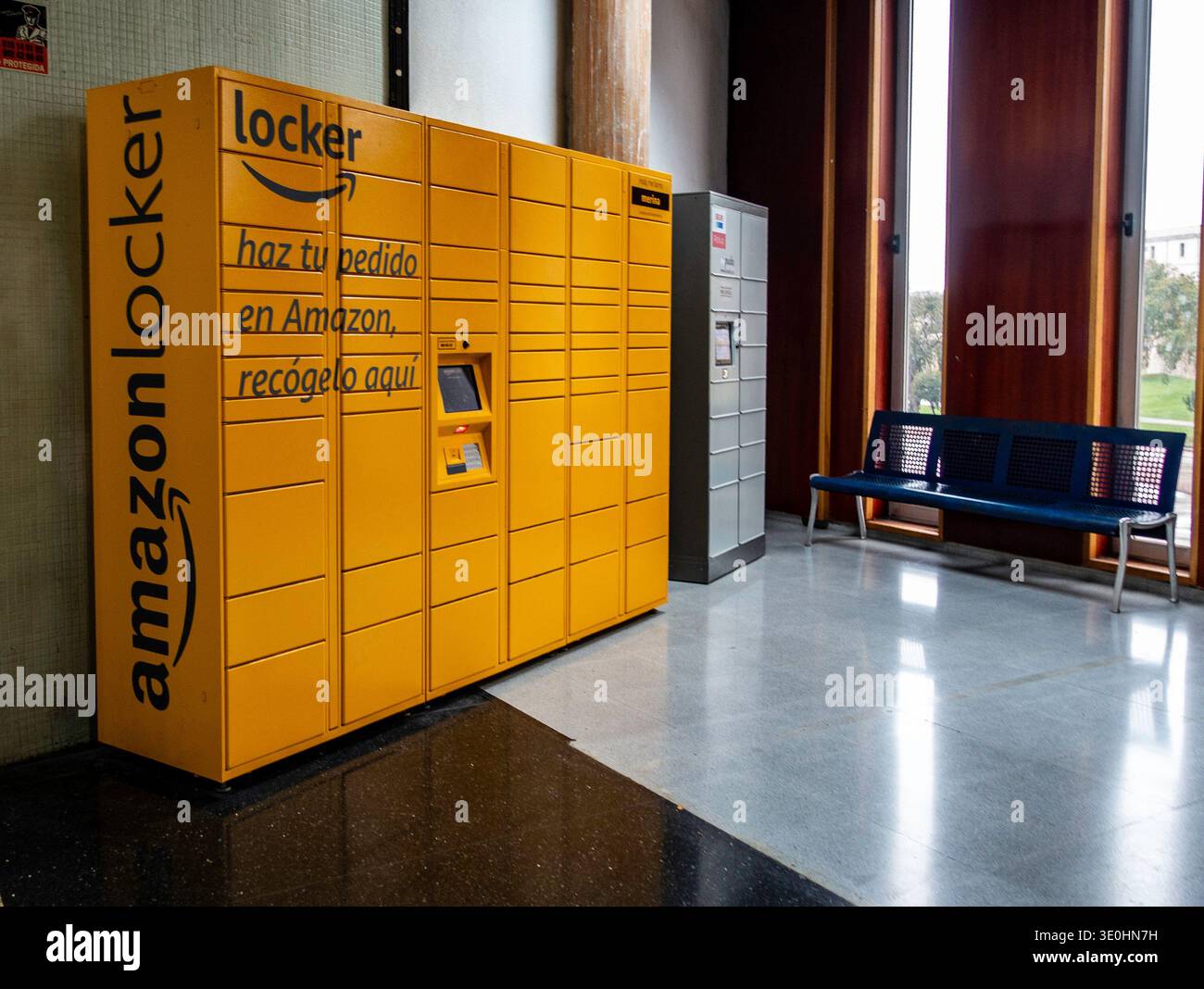 Armadietto giallo Amazon Hub presso la stazione degli autobus di Cartagena, Spagna, situato in un'area d'attesa con una panca in metallo blu e luce naturale dalle grandi finestre. Foto Stock