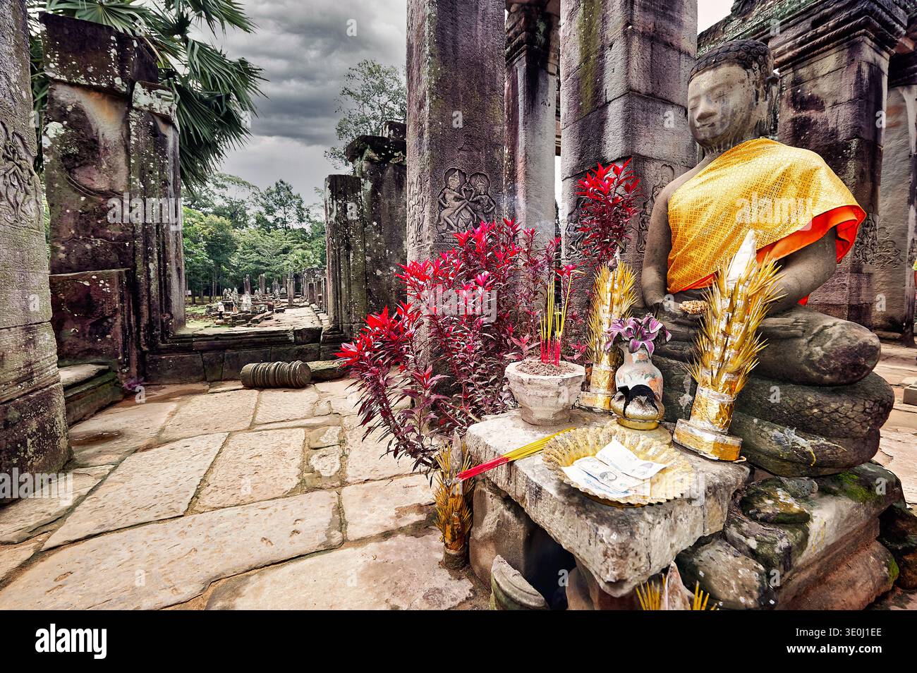 Una statua di Buddha si trova in un antico tempio di Angkor, in Cambogia. Le persone mettono offerte e incenso intorno alla statua. Foto Stock