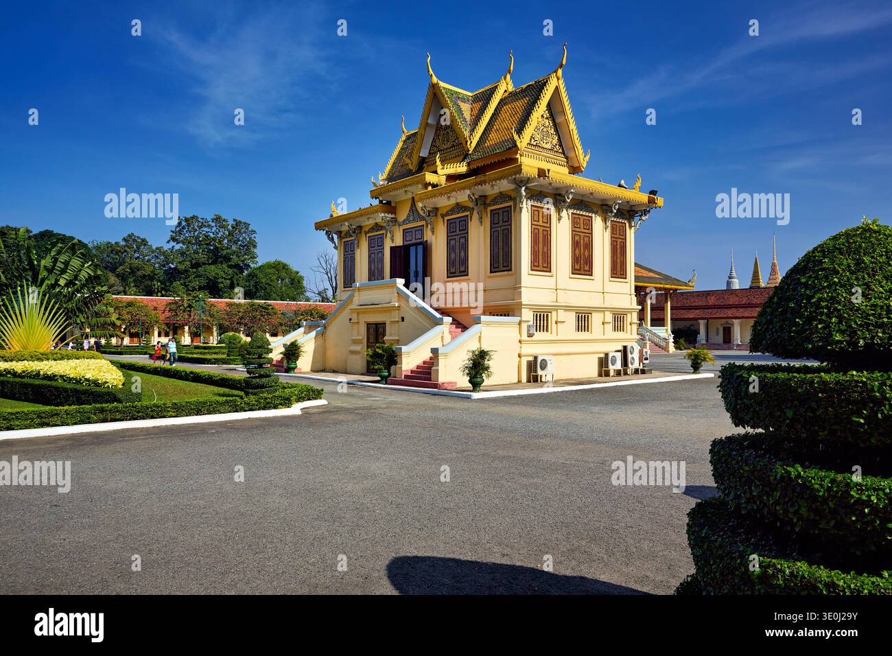 Le persone camminano intorno all'edificio giallo con un tetto dorato al Palazzo reale di Phnom Penh, godendosi i giardini e l'architettura. Foto Stock
