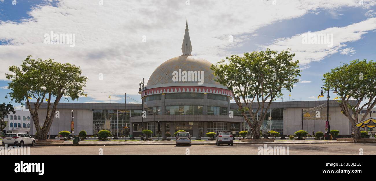 Bandar seri Begawan, Brunei - 24 febbraio 2025: Vista esterna del Museo reale Regalia con la sua caratteristica cupola e guglia sotto un cielo nuvoloso, fiancheggiato da alberi e auto parcheggiate Foto Stock