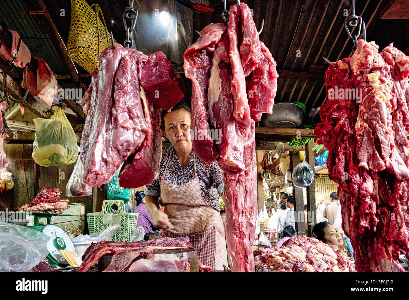 Nel mercato di Phnom Penh, una donna prepara carne cruda per la vendita in mezzo a clienti impegnati. Gestisce il suo stallo pieno di tagli di carne freschi. Foto Stock