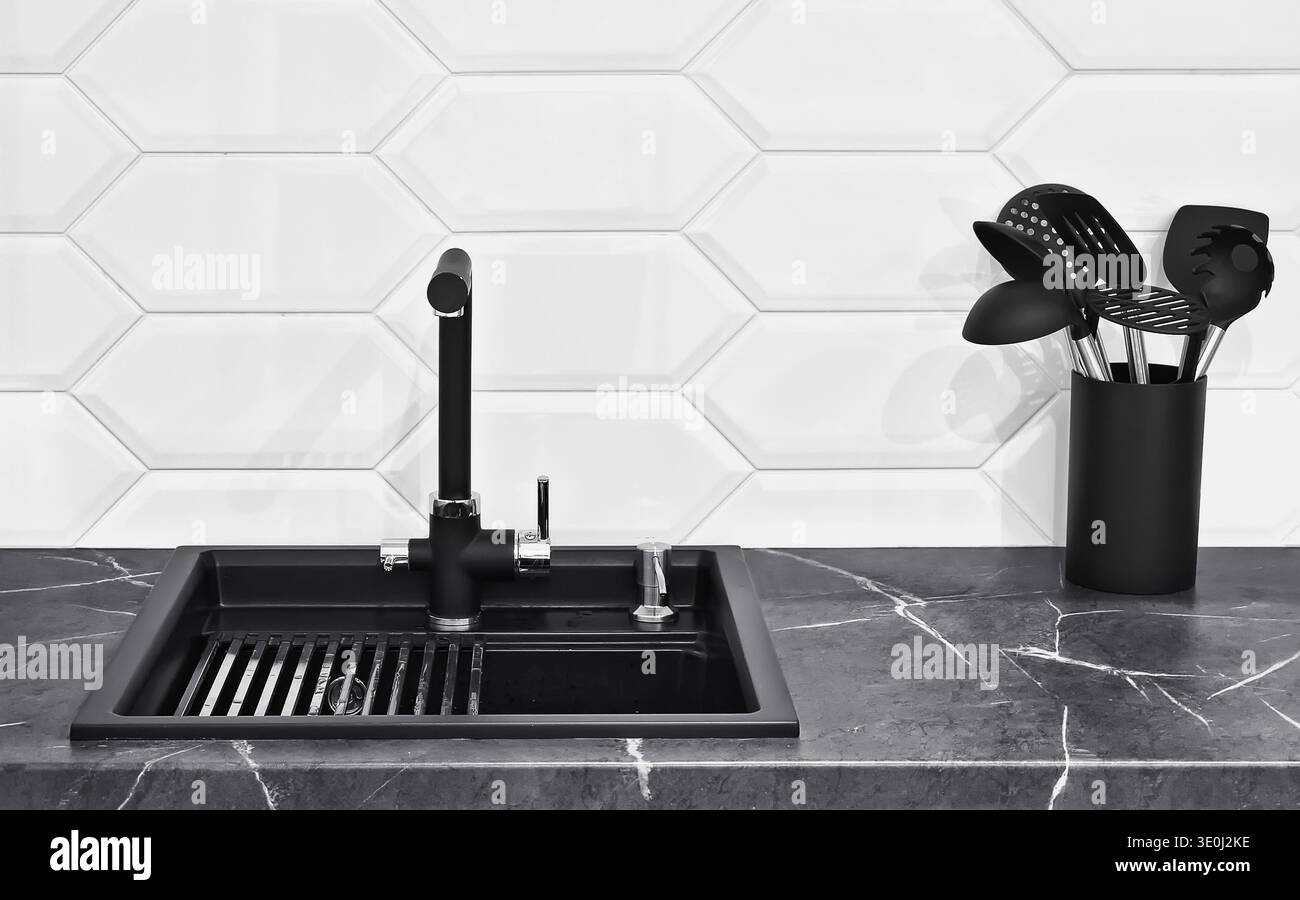 Interni contemporanei della cucina con lavandino nero opaco e rubinetto su ripiano in marmo. Design minimalista per la casa con effetto rovesciamento delle piastrelle esagonali. Foto Stock