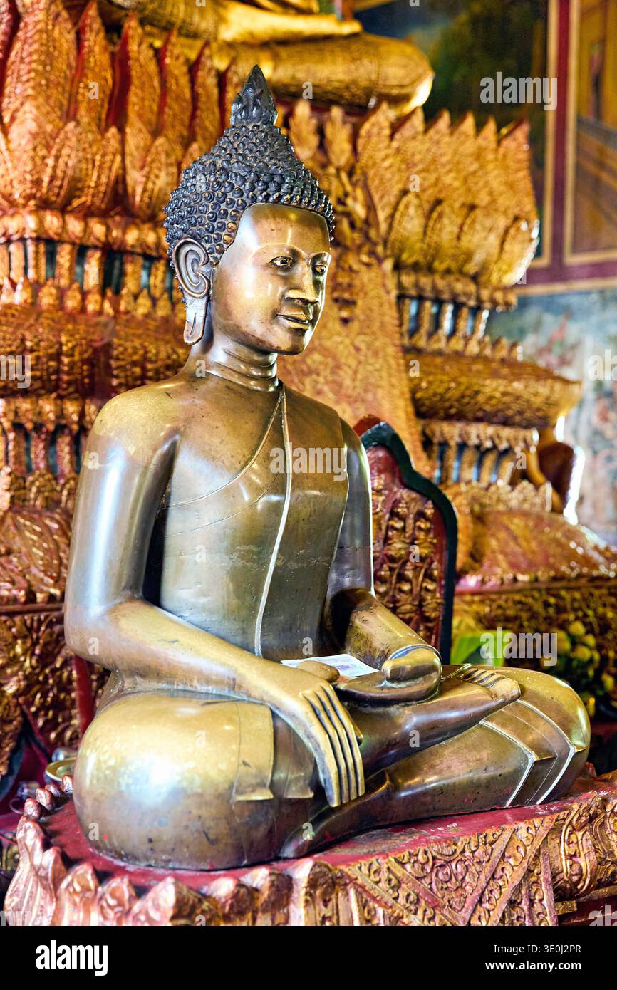 Una statua di Buddha dorata si trova in un tempio cambogiano. I devoti stanno facendo offerte per mostrare rispetto e devozione in questo spazio sacro. Foto Stock