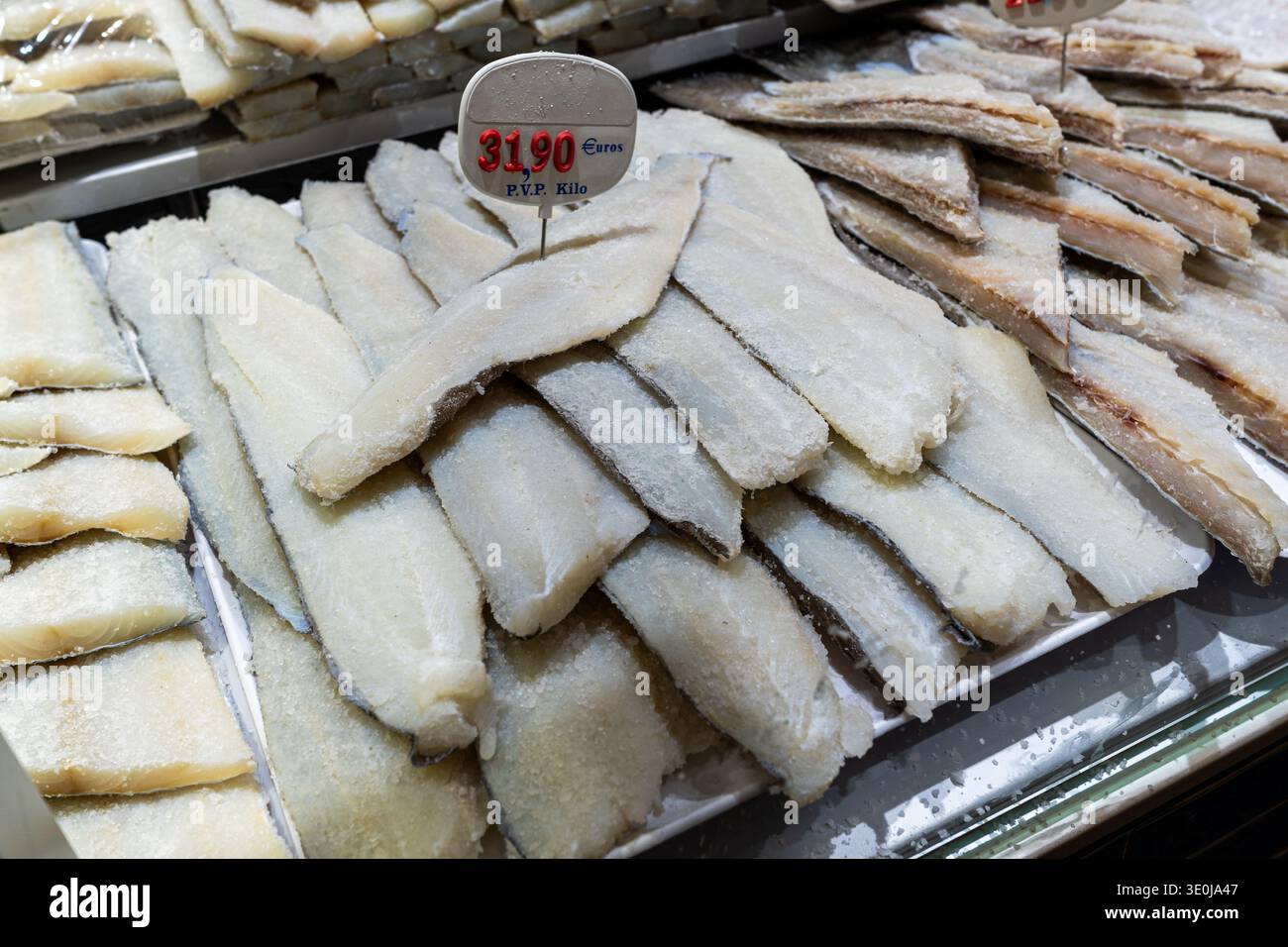 Fette di merluzzo salato esposte su un vassoio presso una bancarella di pesce, perfette per contenuti culinari e blog di ricette tradizionali mediterranee. Foto Stock