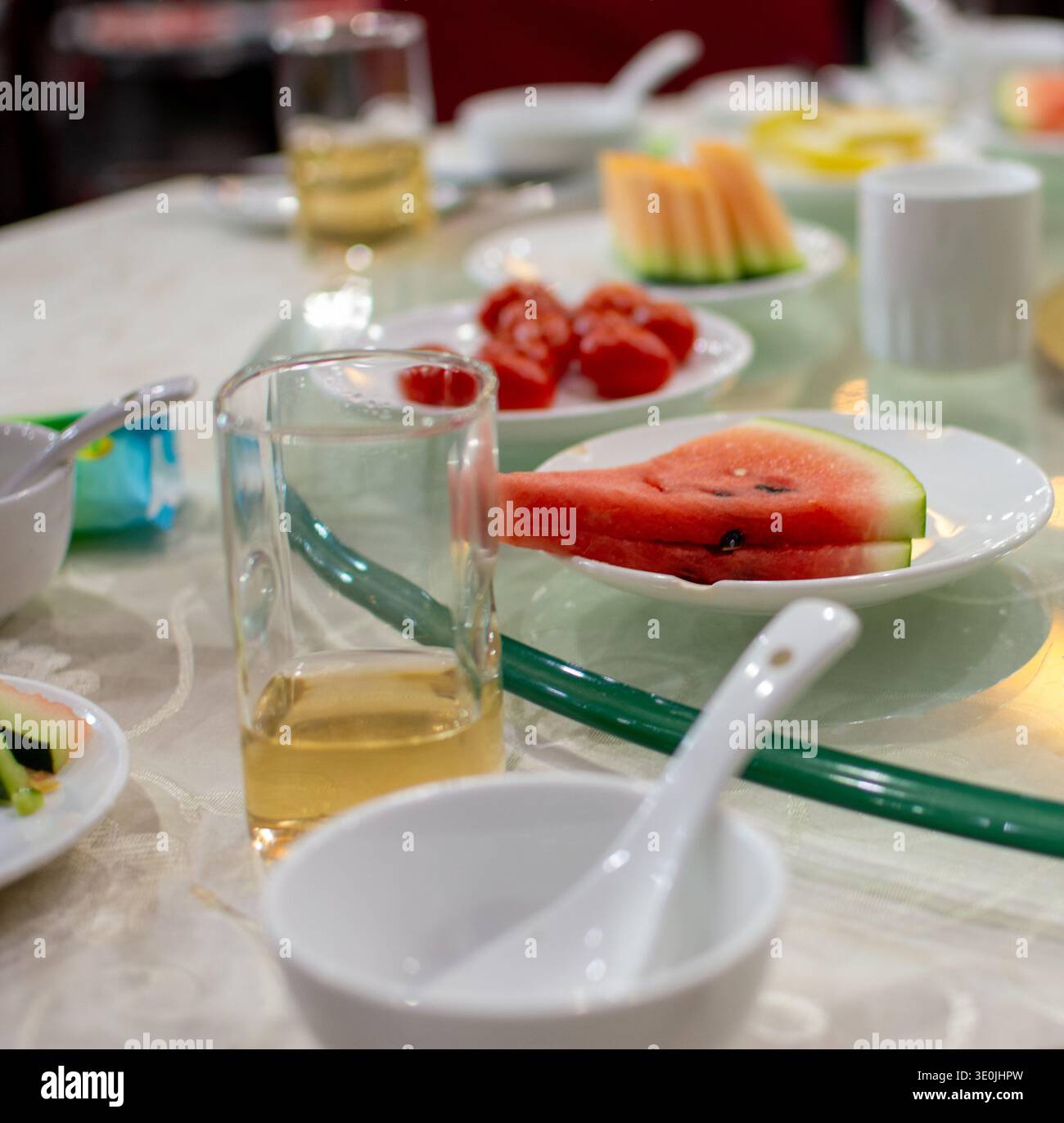 Primo piano di un tavolo da pranzo del ristorante con piatti di frutta fresca, bicchieri da tè e ciotole su una pigra susan di vetro, bassa profondità di campo, pasto informale Foto Stock